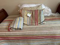 Twin bed made with a comforter, pillow with striped cover, and folded duvet cover and additional bedding items piled at the headboard.