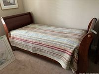 Twin sleighbed frame assembled with multi-colored striped quilt showing headboard, footboard, and side rails from one side angle