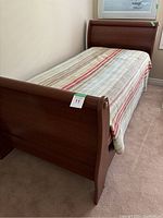 Side angle showing the sleigh bed footboard and mattress with multicolor striped bedspread.