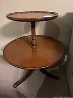 Front view showing two circular tiers with scalloped edges connected by a turned central pedestal and tripod base.