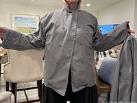 Photo of a gray Chefwear men's chef jacket held by a person, showing front side with buttons and chest pockets.