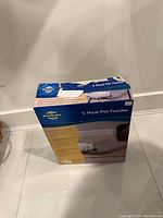 Photo of PetSafe 5 Meal Pet Feeder in box showing front and side panels with branding and usage image.