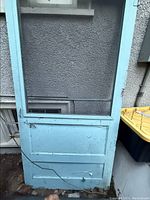 Front view of large antique screen door showing blue frame, wire mesh screen, and three-panel lower wood design with cracks.