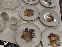 6 antique porcelain plates with detailed fruit motifs and gold trim laid out showing various fruit designs such as grapes, pears, oranges, and apples.
