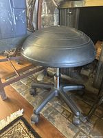 Black Bosu ball chair showing the seating surface, base, and caster wheels from the side.