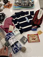 Photo showing assorted new gift items including baby shirt, slippers, scarf, earrings, handkerchief, and small jar.