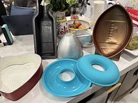Wide shot of cake pans showing football-shaped pan, two blue donut-shaped pans, silver 3D ball pan, and other pans on a white table surface.