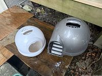 Two dome cat litter boxes placed outdoors on wooden boards with surrounding ground debris.