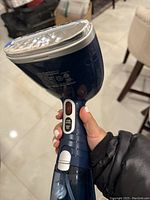 Photo showing a blue Conair handheld clothes steamer with metal steam plate, power switch, and water reservoir held in hand
