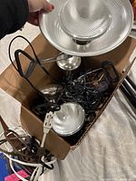 Photo showing floodlights packed inside a cardboard box with visible cords and clips.