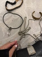 Overview of jewelry and purse including silver chains, black beaded necklace, brass cuff bracelet, and black purse.
