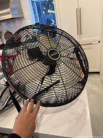 Large black Sunbeam fan with metal blades and protective grill shown from front and side angle on countertop.