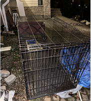 Single extra large black metal wire dog crate with 2 doors and a removable bottom tray, showing overall structure and details of the crate, placed outside on ground near patio bricks.