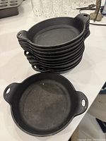 Stack of eleven 6-inch cast iron dishes with two side handles each.