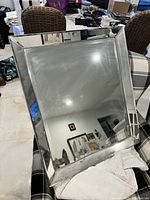 Front view of the rectangular mirror showing the reflective surface and the wide mirrored frame border. Mirror is placed tilted on a cushioned chair.