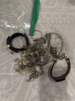 Photo showing various jewelry items including bracelets, chains with pendants, small hoops, and rings on a light patterned fabric.