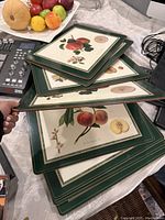 Stack of eight square vintage Pimpernel placemats with green borders showing various fruit botanical illustrations from the Royal Horticultural Society Collection.