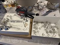 Photo showing two white display boxes filled with metal retail pricing tags and holders, plus one black and red handheld pricing gun tagging machine, all placed on a table.