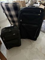 Image showing two black Samsonite suitcases of different sizes positioned side by side on a tiled floor with a patterned chair in the background.