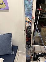 Pair of skis with bindings leaning against wall alongside one set of poles