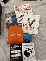 Photo showing all items including Ohuhu hammock pouch, Exercise Anatomy book, Pilates Body book, Pilates Exercises DVD, HEAD sweat tape, Truebuds Sport headphones box, and a blue foam roller.
