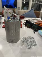 Photo showing Swarovski crystal owl with green eyes, a small dog figurine, and a clear glass turtle, with a silver Swarovski display container.