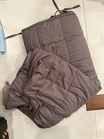 Brown cotton weighted blanket folded showing quilted square pattern and corner ties on tiled floor.
