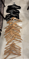 Photo showing a pile of black velvet hangers and multiple wooden hangers laid out on the floor.