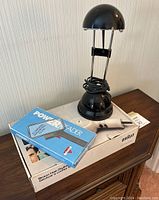 Photo showing the black desk lamp with extendable arms, Braun hair dryer box, and magnifying glass on wooden surface