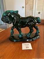 Side view of glossy green glazed ceramic horse figurine on wooden table with auction lot tag visible.