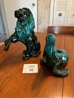Photo showing the Blue Mountain Pottery lion and seal statues together on a wooden table, highlighting size and glaze.