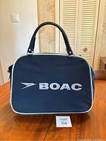 Front view of the navy blue BOAC carry on handbag with white logo and piping on a wooden table.