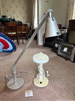 Full view of two crafting lamps on carpet. One tall metal lamp with adjustable arm and weighted base, one small white lamp with discolouration and nick.