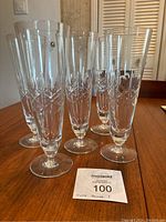 Five clear crystal stemware glasses lined up on a wooden table, displaying cut geometric designs near the bowl bases.