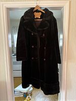 Full view of the dark brown faux fur women's coat hanging on wooden hanger, showing length, collar, and button double-breasted front.