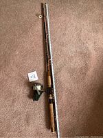 Full fishing rod measured alongside a tape measure showing approx. 7 feet length, rod separated into two pieces, laid flat on carpeted floor.