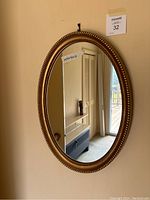 Front view of the oval gold framed mirror hanging on the wall with visible reflection.