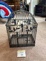 Photo showing full view of ornamental bird cage with top removable and hanging chain hook at the top, placed on carpeted floor.