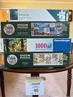 Stack of four puzzle boxes showing brands and puzzle artwork including Indigenous Art by William Monague, Cobble Hill and Ravensburger puzzles