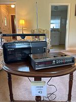 Three radios displayed on a small wood table: large Sony cassette radio with handle and antenna, small Sony radio, and a GE clock radio.