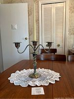 Full view of the three-arm silver candelabra displayed on a table with a lace doily underneath, showing the entire item and its scale.