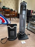 Photo showing two space heaters: a tall tower heater on the right with remote control and a smaller ceramic heater on the left.