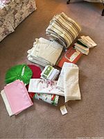Image of assorted folded cloth items: napkins, placemats, and tablecloths in various colors and patterns arranged on carpet.