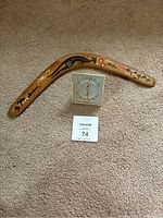 Vintage wooden boomerang with painted Aboriginal-style designs and square humidiguide placed on carpeted floor.