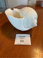 White Wedgwood pottery conch shell vase shown on wooden surface with MaxSold catalog card next to it.