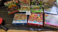 Ten boxed jigsaw puzzles totaling 300 pieces each, arranged on a table showing colorful box art including nature, animals, cartoon figures, and village scenes.
