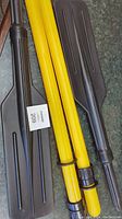 Set of two yellow collapsible kayak paddles with black blades laid out flat showing full length and paddle blade design.