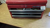 Front view of the Craftsman tool box showing three drawers partially open with contents inside, craftsman logo, and lock with no key.