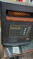 Front view of EdenPURE heater showing the quartz infrared element behind mesh grille, control panel with labeled buttons, and the remote control next to the unit.