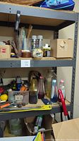 Photo shows metal shelving unit loaded with various containers and spray cans on press board shelves. Shelves adjustable, top shelf missing.